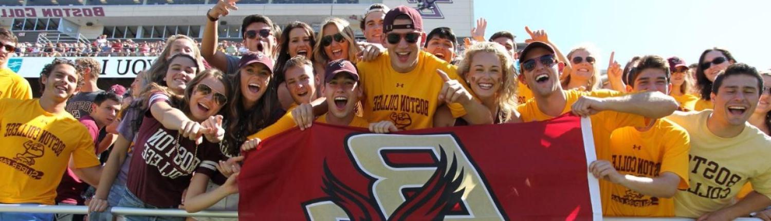 students cheering and holding a BC banner at a football game